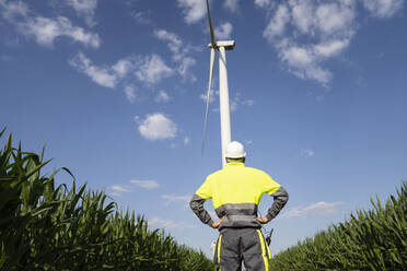 Engineer with hands on hip standing in front of wind turbine - EKGF00489