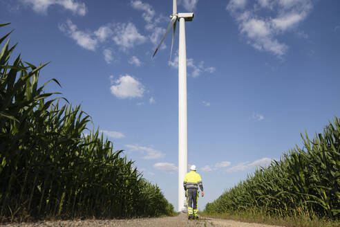 Ingenieur, der an einem sonnigen Tag vor einer Windkraftanlage spazieren geht - EKGF00490