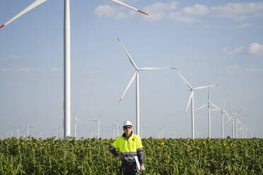 Engineer wearing hardhat standing in front of wind turbines - EKGF00491