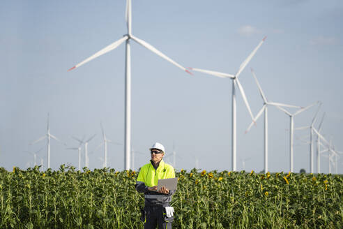Engineer standing with laptop in front of wind turbines - EKGF00493