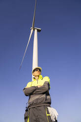 Engineer standing with arms crossed under wind turbine - EKGF00506