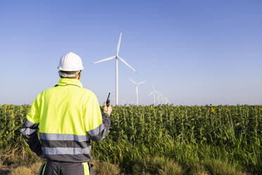 Engineer with walkie-talkie examining wind turbines in field - EKGF00509