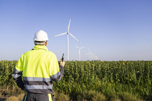 Ingenieur mit Walkie-Talkie bei der Überprüfung von Windkraftanlagen im Feld - EKGF00509