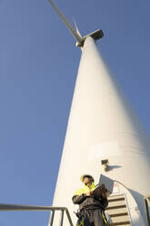 Engineer with laptop standing under wind turbine - EKGF00517