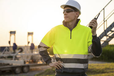 Engineer holding walkie-talkie and standing in field - EKGF00536