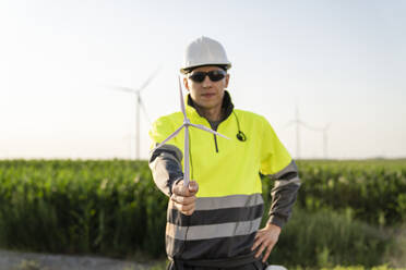 Lächelnder Ingenieur, der ein Windturbinenmodell im Feld hält - EKGF00539