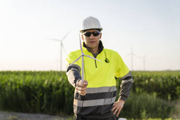 Smiling engineer holding wind turbine model in field - EKGF00539