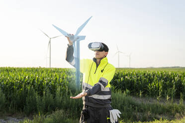 Engineer examining augmented wind turbine model through virtual reality simulator on sunny day - EKGF00542