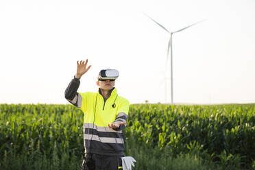 Ingenieur trägt VR-Simulator und gestikuliert im Feld an einem sonnigen Tag - EKGF00547