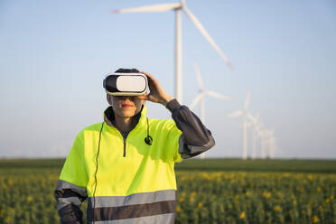 Engineer wearing virtual reality simulator standing in front of wind turbines - EKGF00549