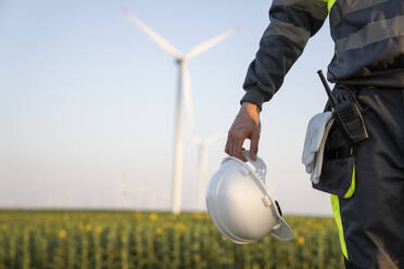 Engineer holding hardhat in front of wind turbines - EKGF00550