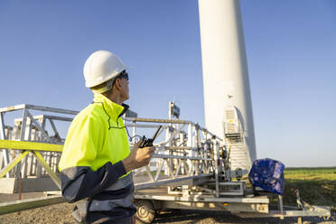 Ingenieur in reflektierender Kleidung bei der Wartungsmaschine einer Windkraftanlage an einem sonnigen Tag - EKGF00554