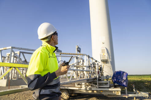 Engineer in reflective clothing by wind turbine maintenance machine on sunny day - EKGF00554