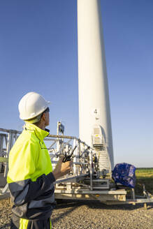 Ingenieur, der an einem sonnigen Tag die Wartungsmaschine einer Windkraftanlage betrachtet - EKGF00555