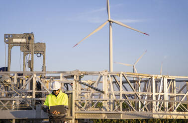 Engineer using laptop in front of wind turbine maintenance machine - EKGF00566