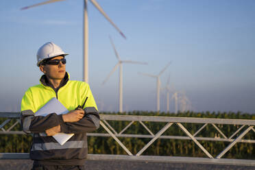 Engineer in reflective clothing and hardhat at wind turbine field - EKGF00572