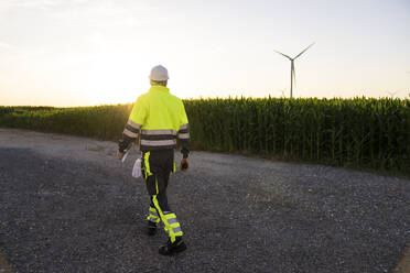 Engineer walking on street by field with wind turbines - EKGF00575