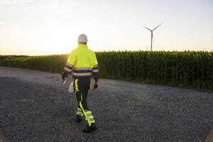 Ingenieur geht auf der Straße neben einem Feld mit Windturbinen - EKGF00575