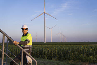 Engineer with laptop moving up on steps by wind turbines - EKGF00579