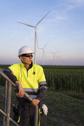 Ingenieur lehnt an einem Geländer vor einem Windkraftanlagenpark - EKGF00584
