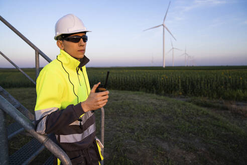 Engineer wearing reflective clothing by wind turbine field - EKGF00585