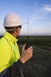 Ingenieur mit Walkie-Talkie bei der Betrachtung einer Windkraftanlage in einem Bauernhof - EKGF00586