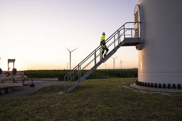 Engineer moving up on steps by wind turbine farm - EKGF00587