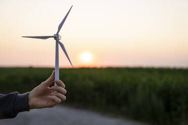 Hand eines Ingenieurs mit Modell einer Windkraftanlage bei Sonnenuntergang - EKGF00593