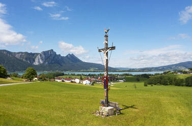 Österreich, Oberösterreich, Loibichl, Kruzifix vor Seeuferdorf im Sommer - WWF06335