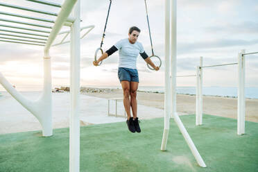 Sportive and athletic man doing functional training exercise at the outdoor gym - Adult athlete doing workout at sunrise at calisthenics park on the beach - Fitness, healthy lifestyle and sport concepts - DMDF04363