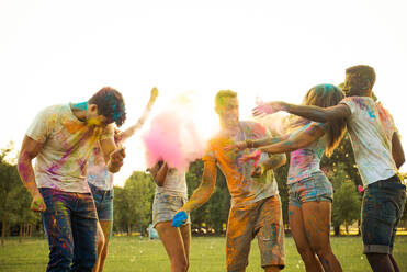 Group of happy friends playing with holi colors in a park - Young adults having fun at a holi festival, concepts about fun, fun and young generation - DMDF04396