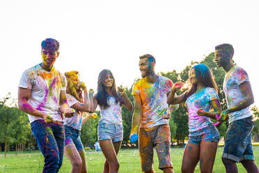 Group of happy friends playing with holi colors in a park - Young adults having fun at a holi festival, concepts about fun, fun and young generation - DMDF04397