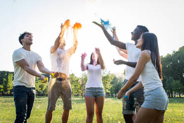 Group of happy friends playing with holi colors in a park - Young adults having fun at a holi festival, concepts about fun, fun and young generation - DMDF04400