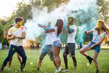 Group of happy friends playing with holi colors in a park - Young adults having fun at a holi festival, concepts about fun, fun and young generation - DMDF04404