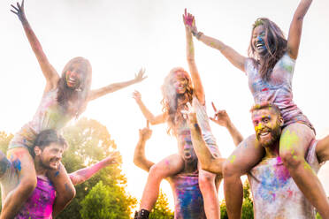 Group of happy friends playing with holi colors in a park - Young adults having fun at a holi festival, concepts about fun, fun and young generation - DMDF04414