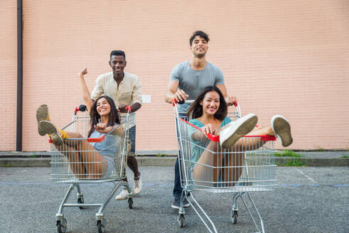 Multi-ethnic group of friends playing with shopping carts in a parking - DMDF04415