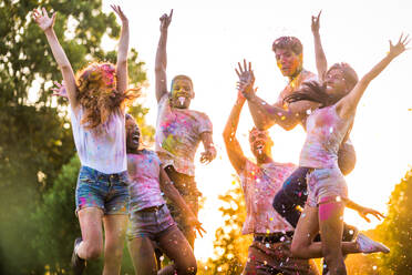 Group of happy friends playing with holi colors in a park - Young adults having fun at a holi festival, concepts about fun, fun and young generation - DMDF04417