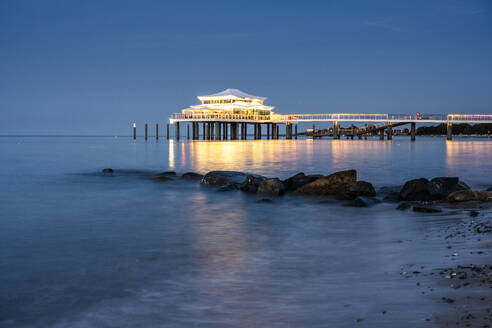 Deutschland, Schleswig-Holstein, Timmendorfer Strand, Küstenfelsen in der Abenddämmerung mit beleuchtetem Mikado-Teehaus im Hintergrund - EGBF00924