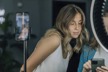 Hairdresser showing smart phone to customer in hair salon - EVKF00039