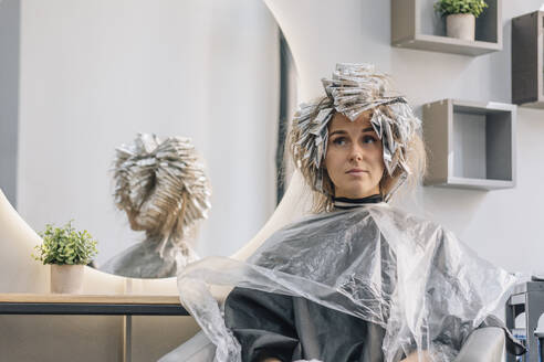 Thoughtful woman sitting with foil on hair at salon - EVKF00043