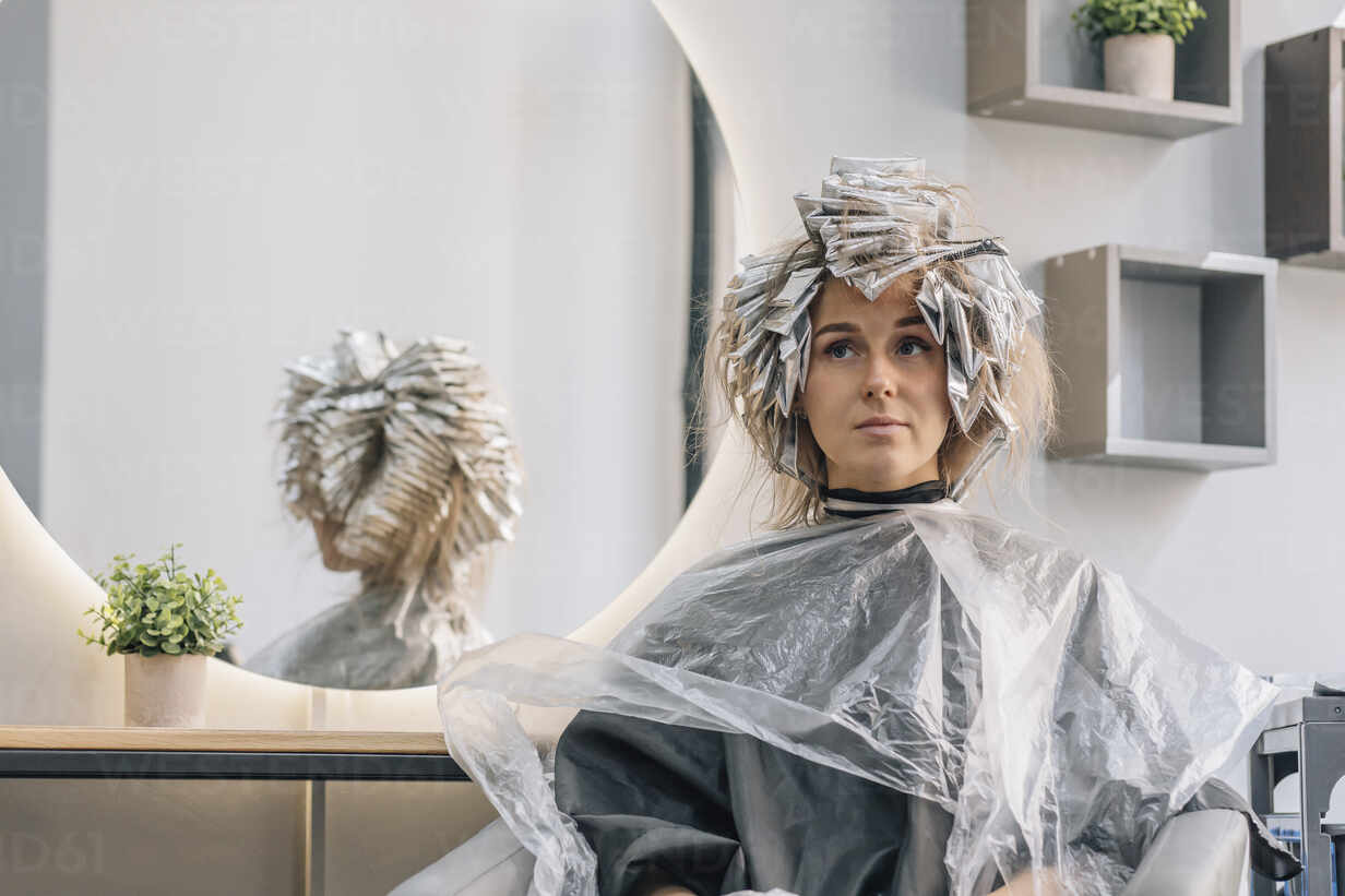 Thoughtful woman sitting with foil on hair at salon stock photo