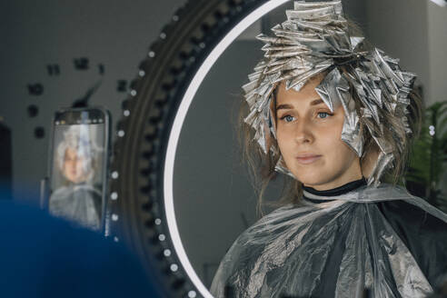 Reflection of woman with foil on hair in mirror at salon - EVKF00044