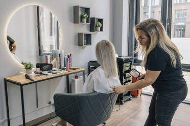 Hairdresser holding hairbrush and examining customer's hair in salon - EVKF00047