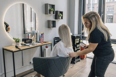 Friseurin, die eine Haarbürste hält und das Haar eines Kunden im Salon untersucht - EVKF00047