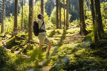 Hiker with arms outstretched standing in forest - DIGF20520