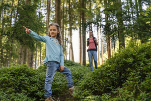 Girl pointing and mother walking from behind in forest - DIGF20529
