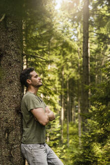 Mann mit verschränkten Armen lehnt an einem Baum im Wald - DIGF20530