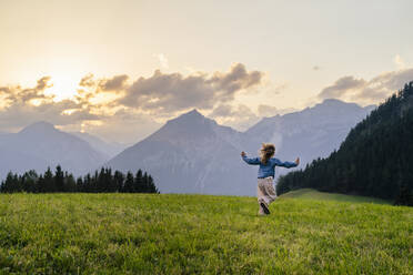 Mädchen läuft auf Gras vor Bergen bei Sonnenuntergang - DIGF20533