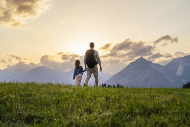 Vater und Tochter wandern auf einer Wiese in den Bergen bei Sonnenuntergang - DIGF20534