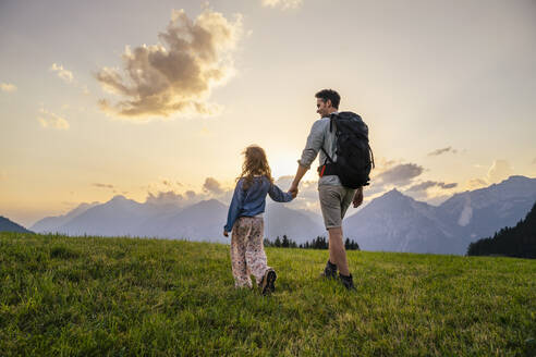 Vater erkundet mit Tochter auf einer Wiese bei Sonnenuntergang - DIGF20536